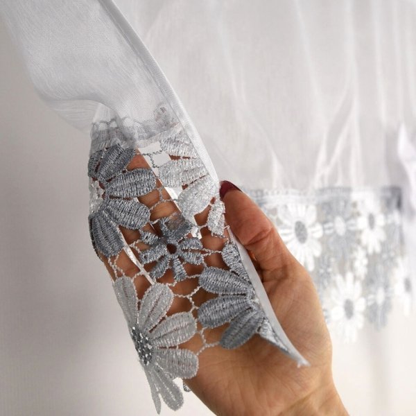 Detal szarego haftu gipiurowego z motywem kwiatowym trzymanego w dłoni, zdobiącego firankę Megan