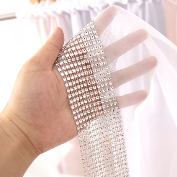 Prezentacja transparentności tkaniny woalowej oraz lśniących detali cyrkonii na dłoni.